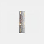 A white Clérachic wall light with a chiselled, cracked surface and light shining through the fissures, on a pale backdrop.