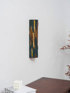 From a slight angle, a Clérachic Bark wall light with a glowing slit hangs on a white wall above a white cube candle and a wooden table.