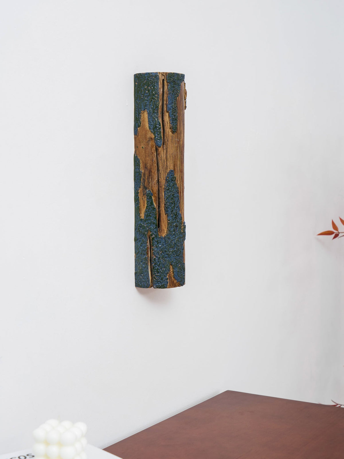 Close to the top of a wooden table, a Clérachic Bark wall light shows its blue-grey bark texture against a white wall.