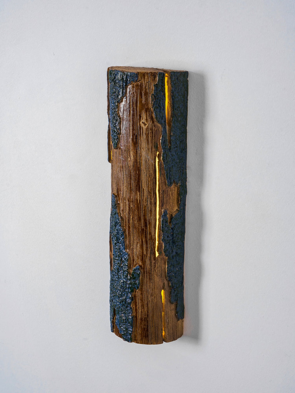A Clérachic Bark wall light seen slightly from the side, with a golden light line glowing down the middle of the wood.