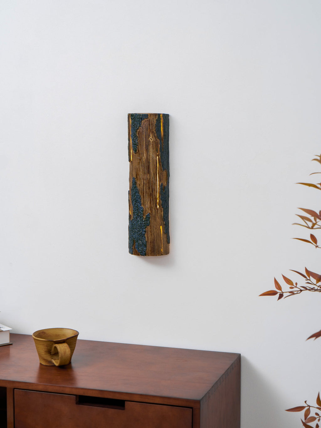 A small-in-frame Clérachic Bark wall light on a white wall above a wooden drawer unit, a ceramic cup and red-brown leaves.