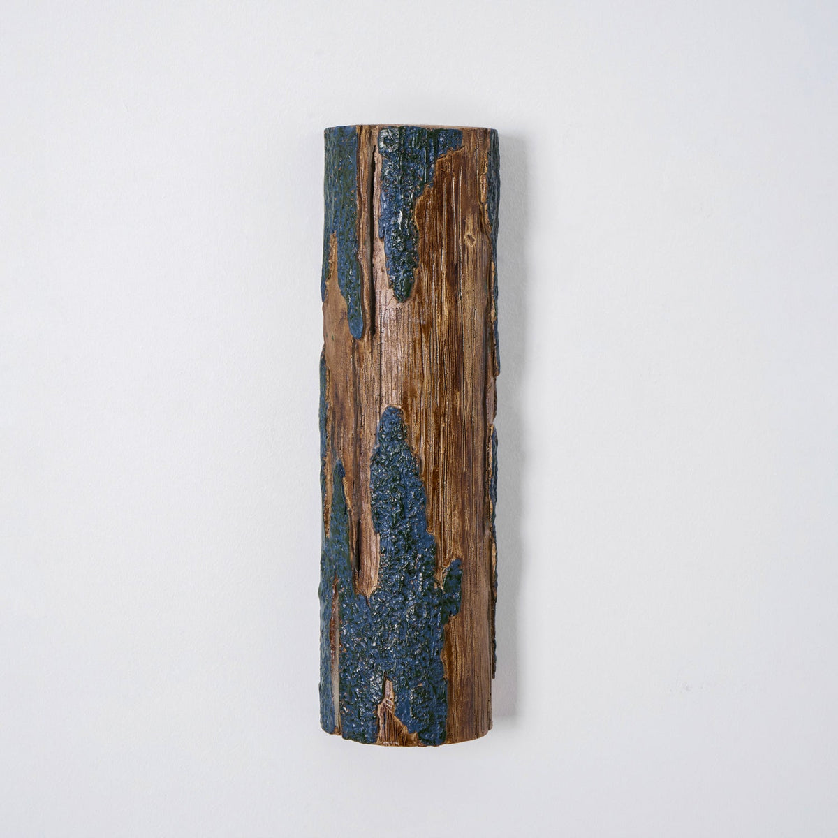 Straight-on view of an unlit Clérachic Bark wall light, with wood grain and a knot between two bands of blue-grey bark.