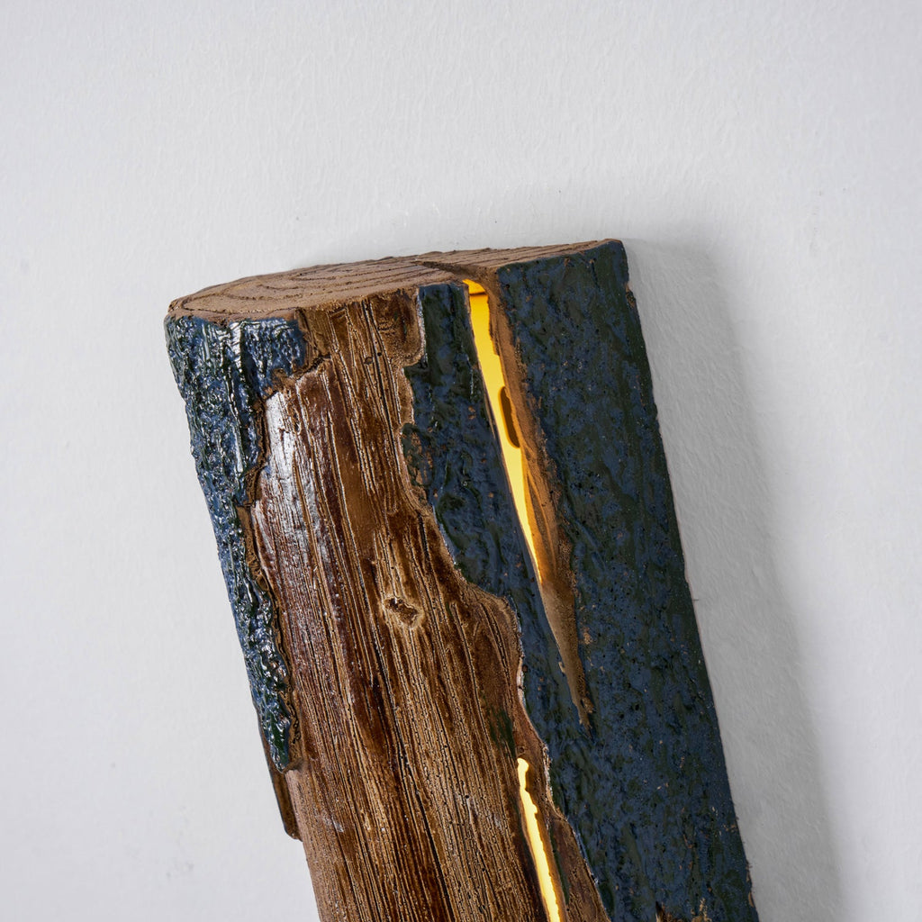 Close view of the top end of a Clérachic Bark wall light, showing the cut wood ring, the bark edge and the light glowing in the slit.