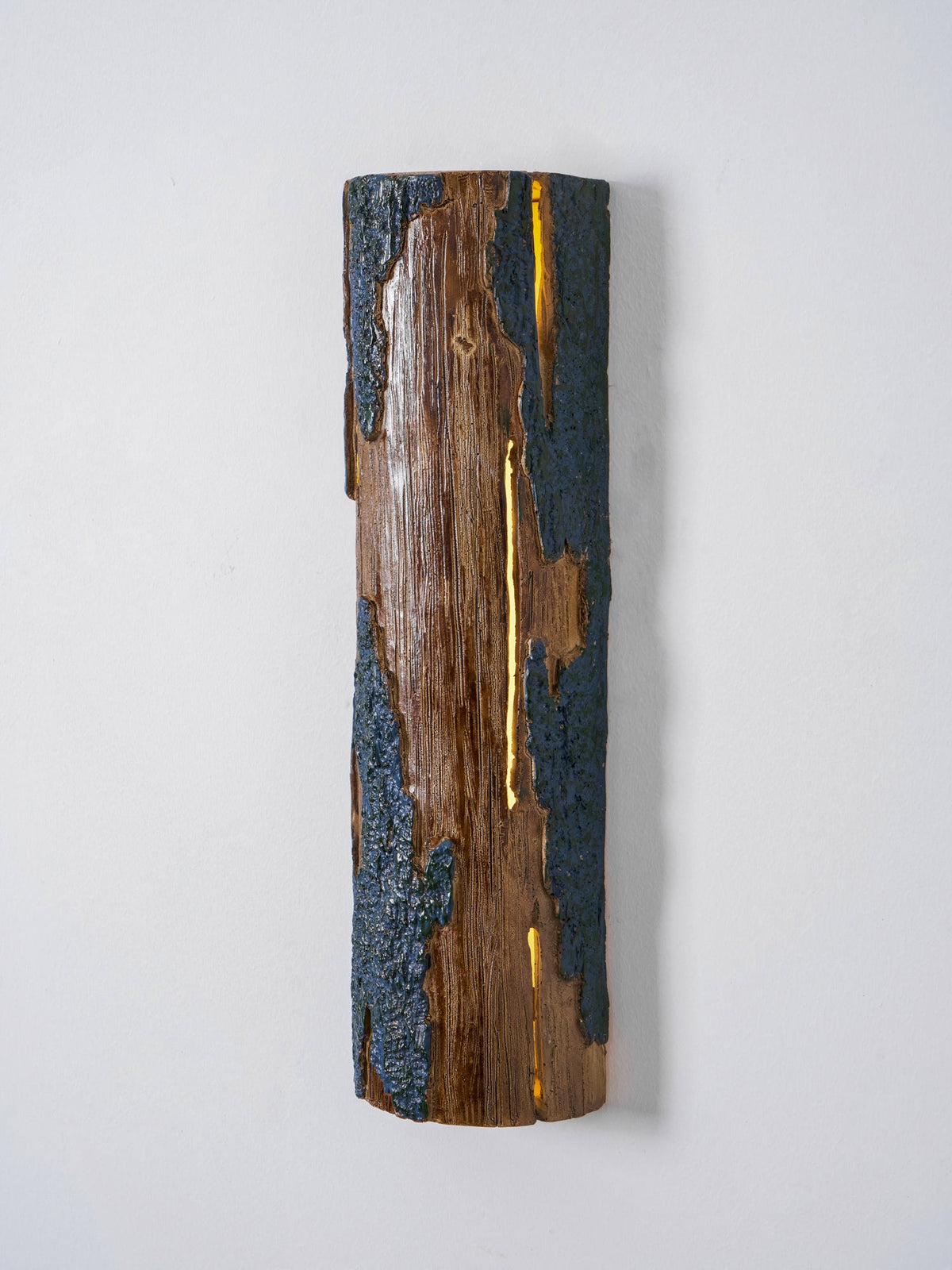 Front view of a Clérachic Bark wall light with a narrow glowing slit down the wood and a bark texture along the edges.