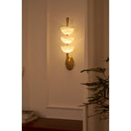 Clérachic triple-dome sconce lit in a dim corner, warm light washing up and down the wall from the three alabaster bowls.