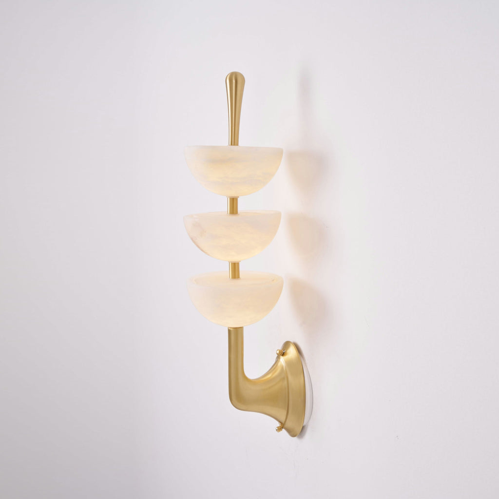 Three-quarter view of the Clérachic triple-dome wall sconce, the brass arm curving out from the wall to carry the stone bowls.