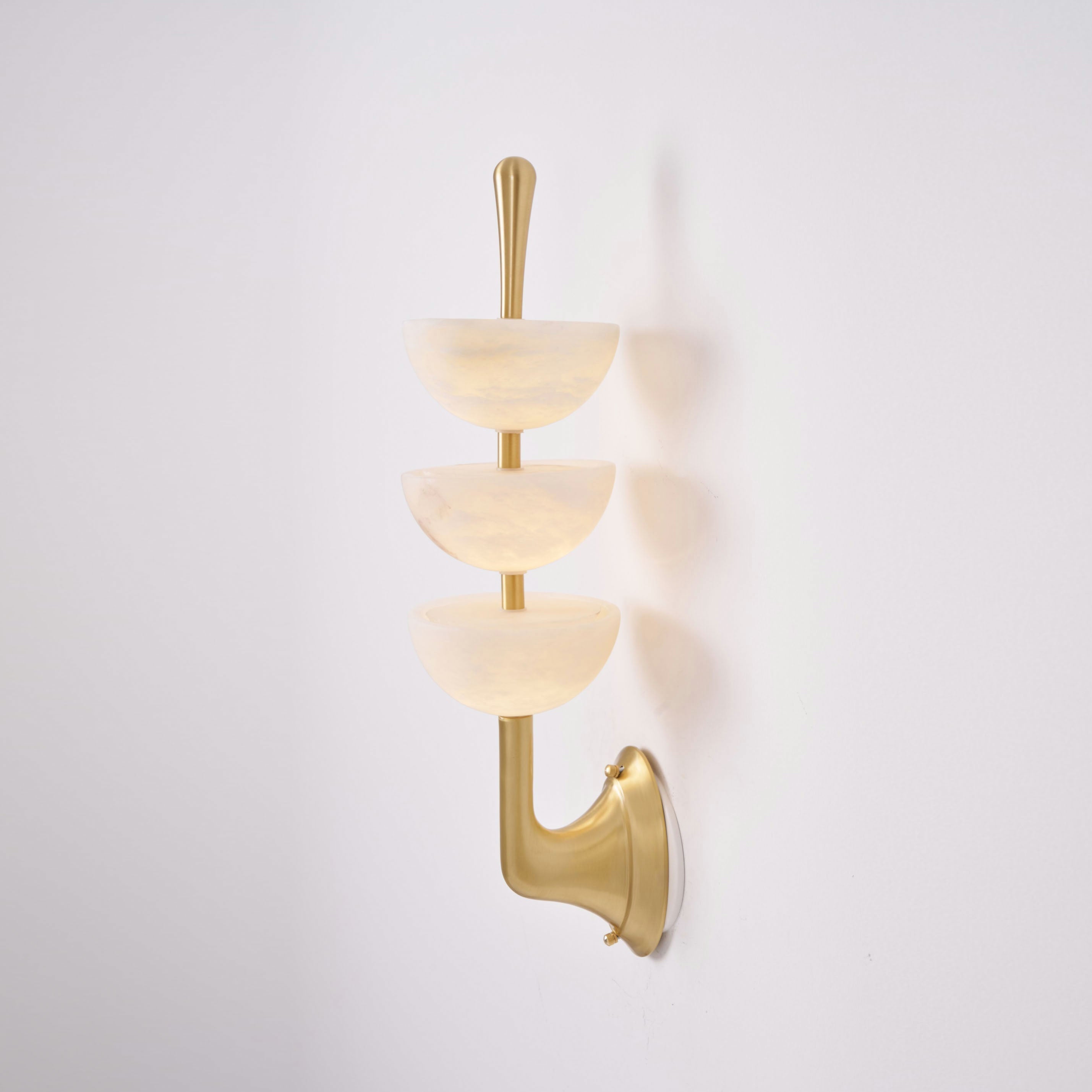Three-quarter view of the Clérachic triple-dome wall sconce, the brass arm curving out from the wall to carry the stone bowls.