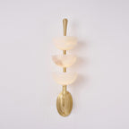 Clérachic alabaster wall sconce head-on, one bowl carrying a darker rust-grey vein of its own against the warm off-white stone.