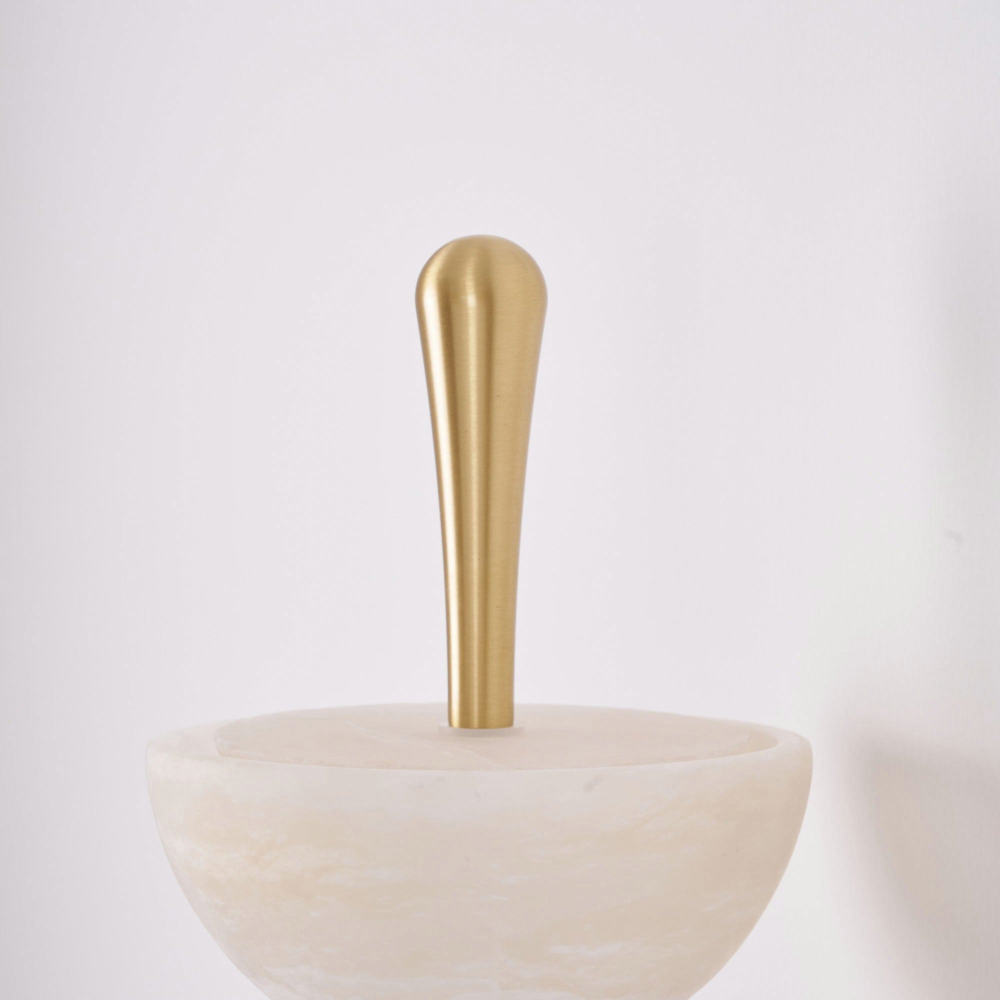 Close-up of the brass teardrop finial on the Clérachic alabaster wall sconce, seated on the rim of the topmost stone bowl.