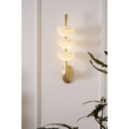 The Clérachic alabaster wall sconce lit on a tall panelled wall, its slim body taking a narrow run a wide fixture would fill.