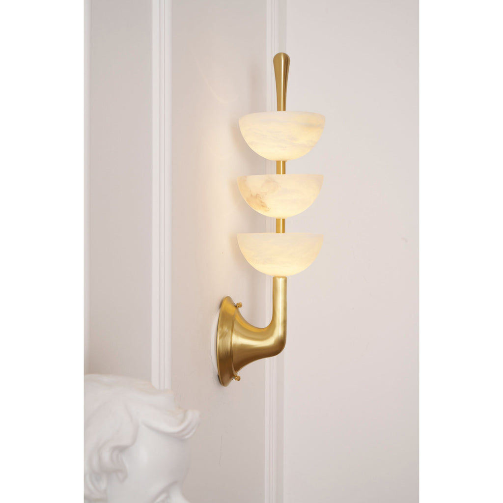 Angled view of the lit Clérachic wall sconce beside a plaster bust, brass arm and backplate catching the light on the wall.