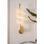 Clérachic triple-dome wall sconce lit beside a trailing houseplant, warm glow held inside the three stacked alabaster bowls.