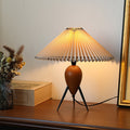 Lit Clérachic table lamp on a dark wood sideboard, its pleated shade glowing warm beside dried flowers and a gold frame.