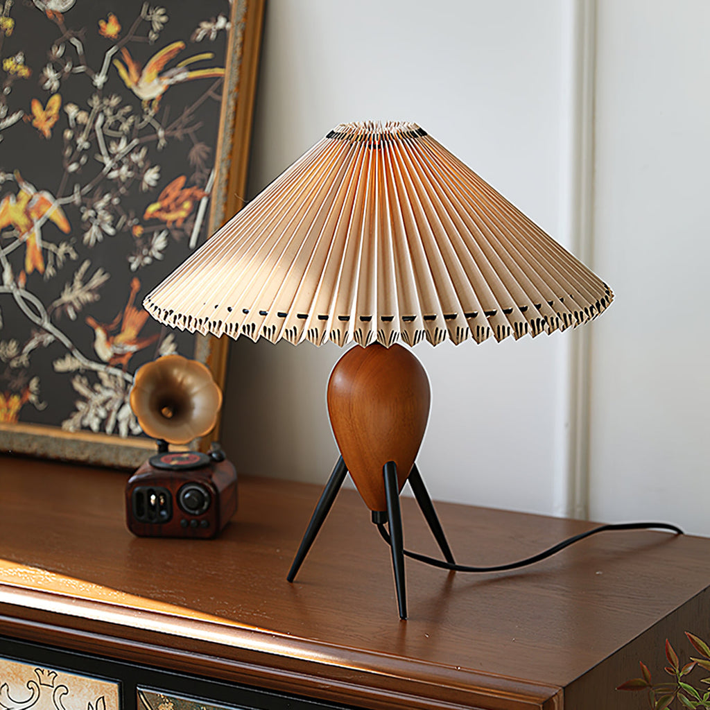Pleated-shade Clérachic table lamp glowing on a dark wood cabinet, with a bird-print panel and a small retro radio behind.