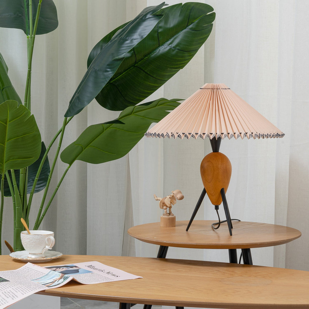 This Clérachic table lamp sits low on a round wooden table, framed by large green leaves and a folded newspaper.