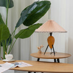 This Clérachic table lamp sits low on a round wooden table, framed by large green leaves and a folded newspaper.
