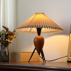 Warm light spills from the pleated shade of this Clérachic table lamp, set beside dried flowers on a dark wood shelf.