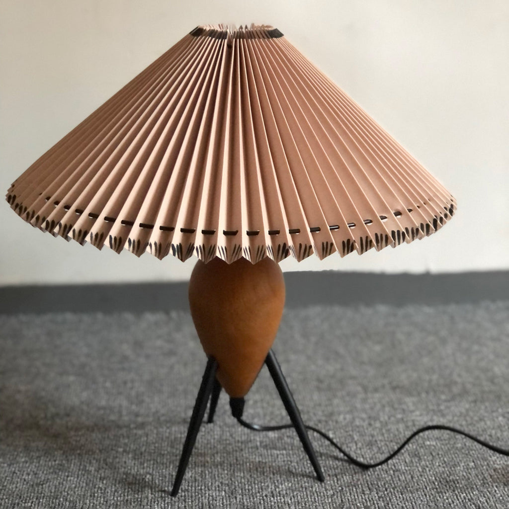 Low-angle view of a Clérachic table lamp on grey carpet, its wide pleated shade tilted toward the camera and unlit.