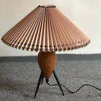 Low-angle view of a Clérachic table lamp on grey carpet, its wide pleated shade tilted toward the camera and unlit.