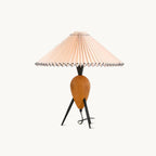 Straight-on studio view of a Clérachic table lamp, the pleated shade wide above a wood teardrop base and three black legs.