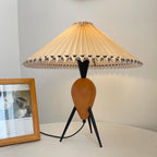 A Clérachic table lamp on a low table, lit, beside a wooden picture frame and white wall.