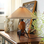 Bright light falls on this Clérachic table lamp on a dark wood cabinet, with a framed bird print and ceramic figures behind.
