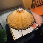 Seen from above, the pleated shade of this Clérachic table lamp spreads wide over a bedside table with a pink cushion.