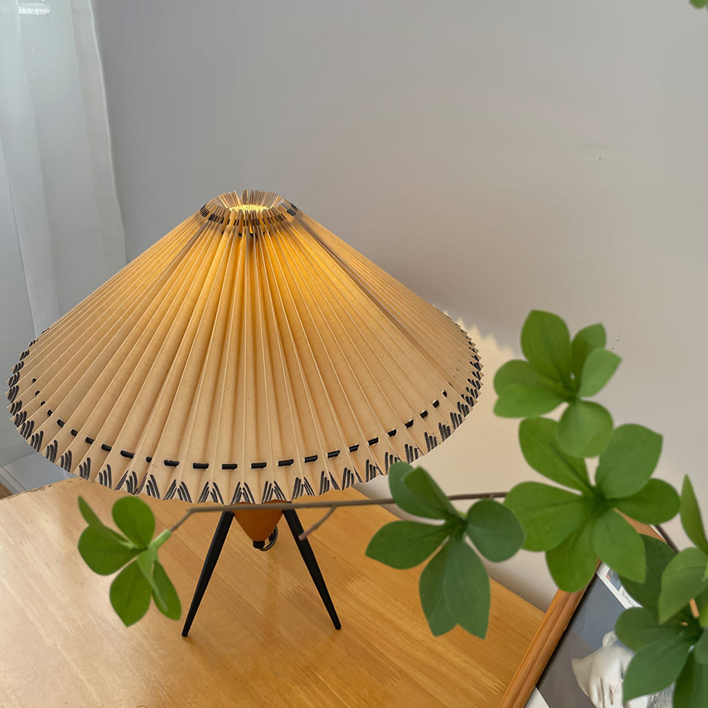 Green clover leaves frame this Clérachic table lamp, its pleated shade glowing over a light wood tabletop.