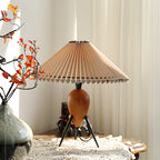 This Clérachic table lamp sits by a window with orange autumn sprigs and a lace runner, soft curtains behind.