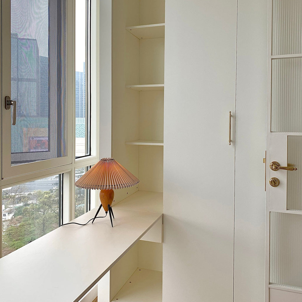 Small in a bright corner, this Clérachic table lamp sits on a window ledge beside a white built-in cabinet and a door.