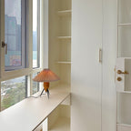 Small in a bright corner, this Clérachic table lamp sits on a window ledge beside a white built-in cabinet and a door.