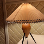 Close crop of the pleated shade and upper wood base of this Clérachic table lamp, against a quilted cream wall.