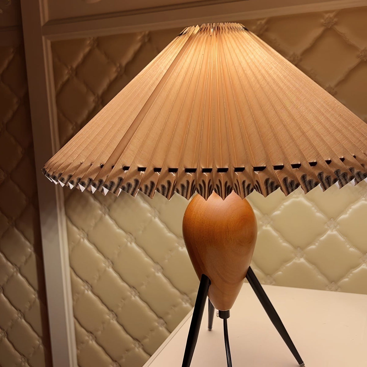 Close crop of the pleated shade and upper wood base of this Clérachic table lamp, against a quilted cream wall.