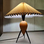 With its shade tilted slightly, this Clérachic table lamp glows warm on grey carpet against a grey wall.