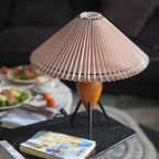 This Clérachic table lamp on a black wood tray, beside a colourful book and a plate of fruit and salad in soft focus.