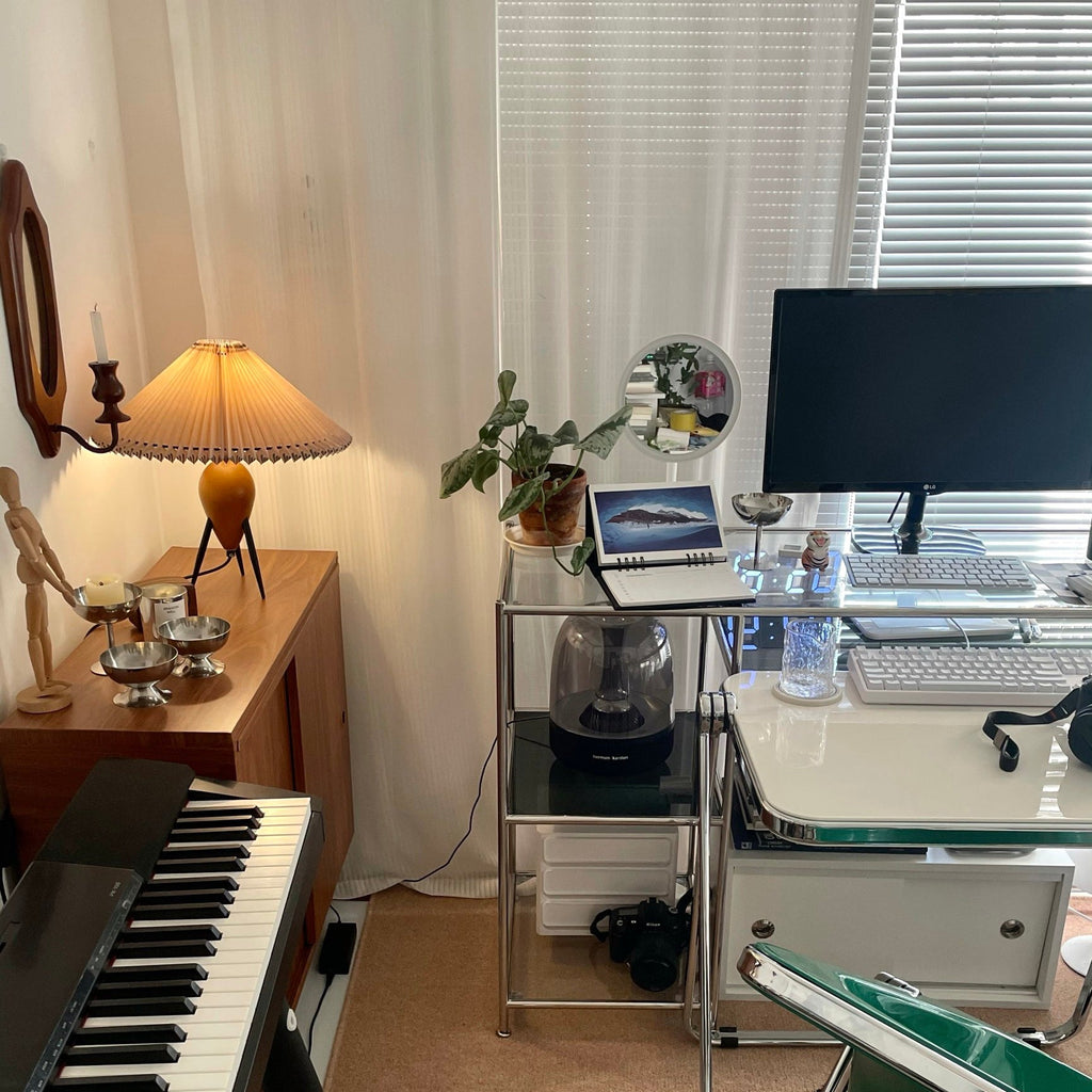 A Clérachic table lamp lights a corner of a studio, with a keyboard, a desk setup and a wall candle holder beyond.