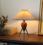 A lit Clérachic table lamp with warm light on a dark wood shelf, flowers to the left and a tall gold frame to the right.