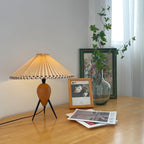Beside a framed photo and a leafy glass vase, this Clérachic table lamp stands on a light wood table with magazines.
