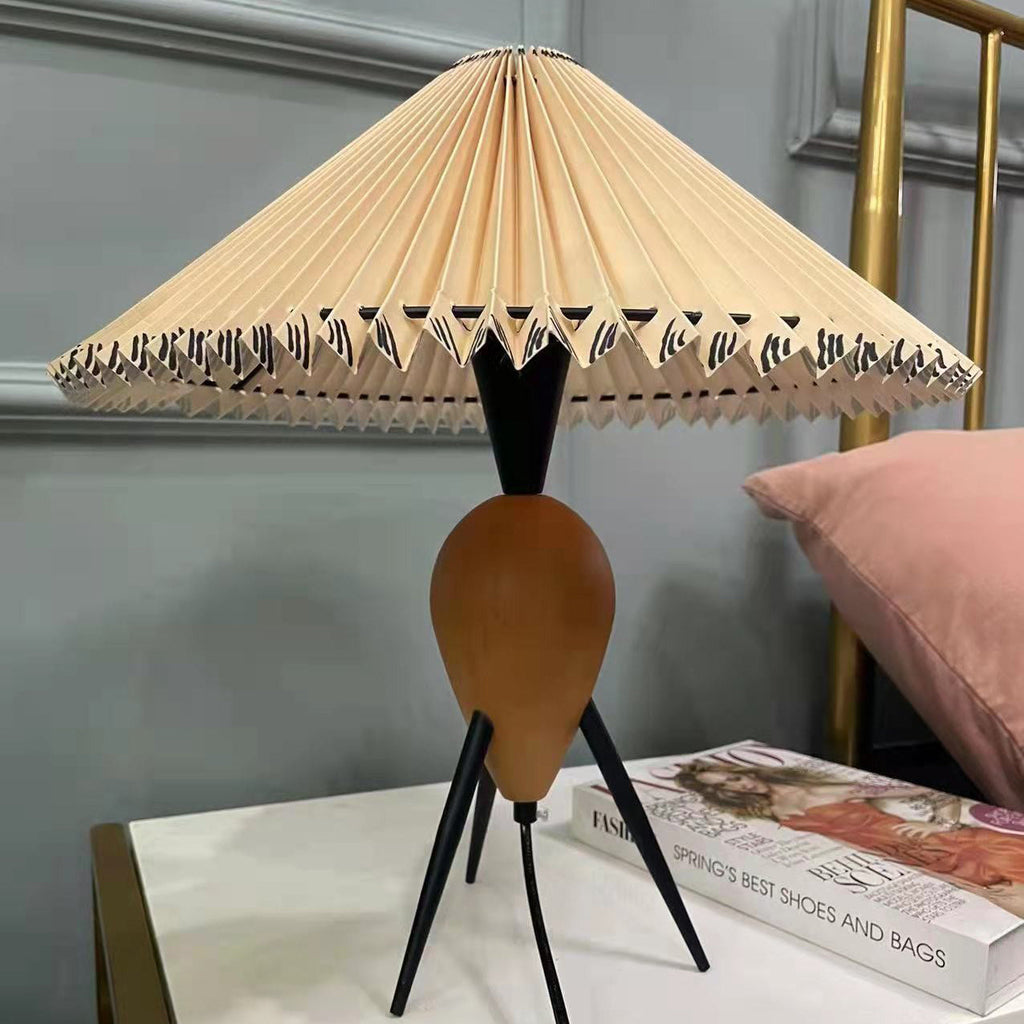The black legs and wood base of this Clérachic table lamp stand out against a pink cushion and a white shelf with a magazine.