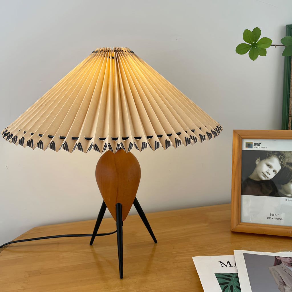 A Clérachic table lamp on a honey-toned desk, a framed portrait beside it and the black cord running off the edge.