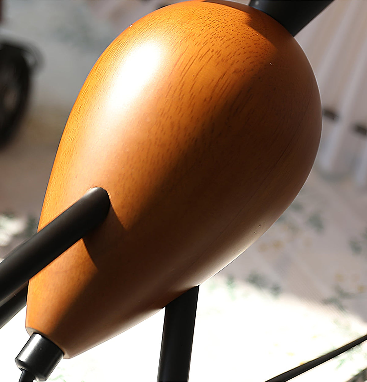 Close view of the smooth, grained wood teardrop base and a black tripod leg of this Clérachic table lamp.
