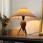 Soft side light on a Clérachic table lamp on a wood shelf, with dried flowers, a pale box and a gold frame behind.