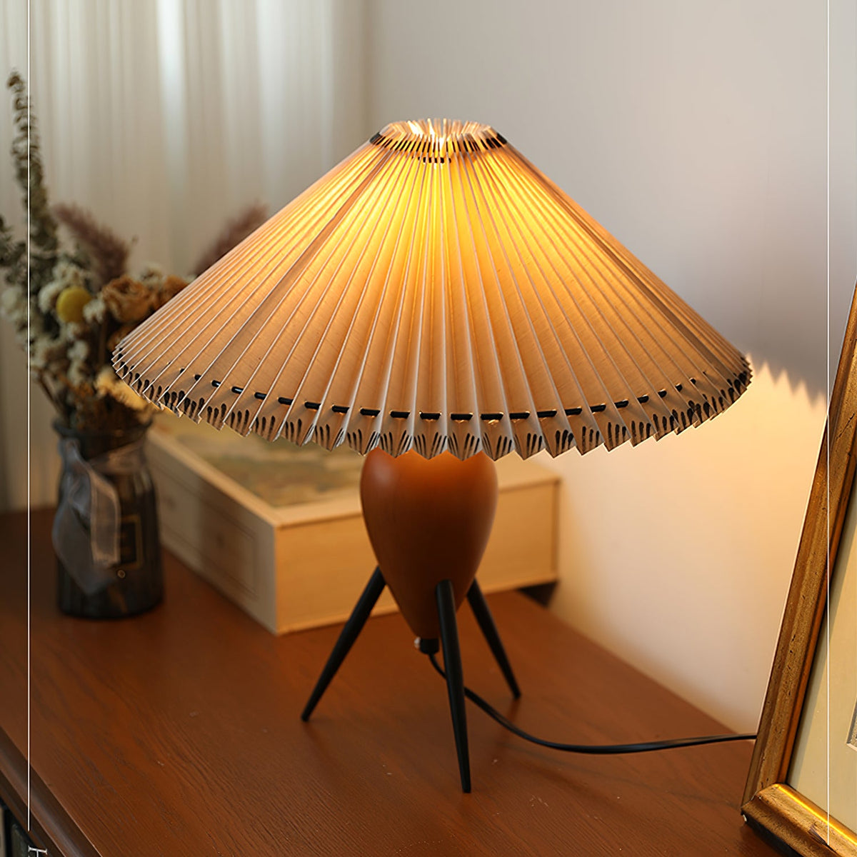 Warm light glows through the shade of this Clérachic table lamp as it stands on a wood desk beside a gold frame.