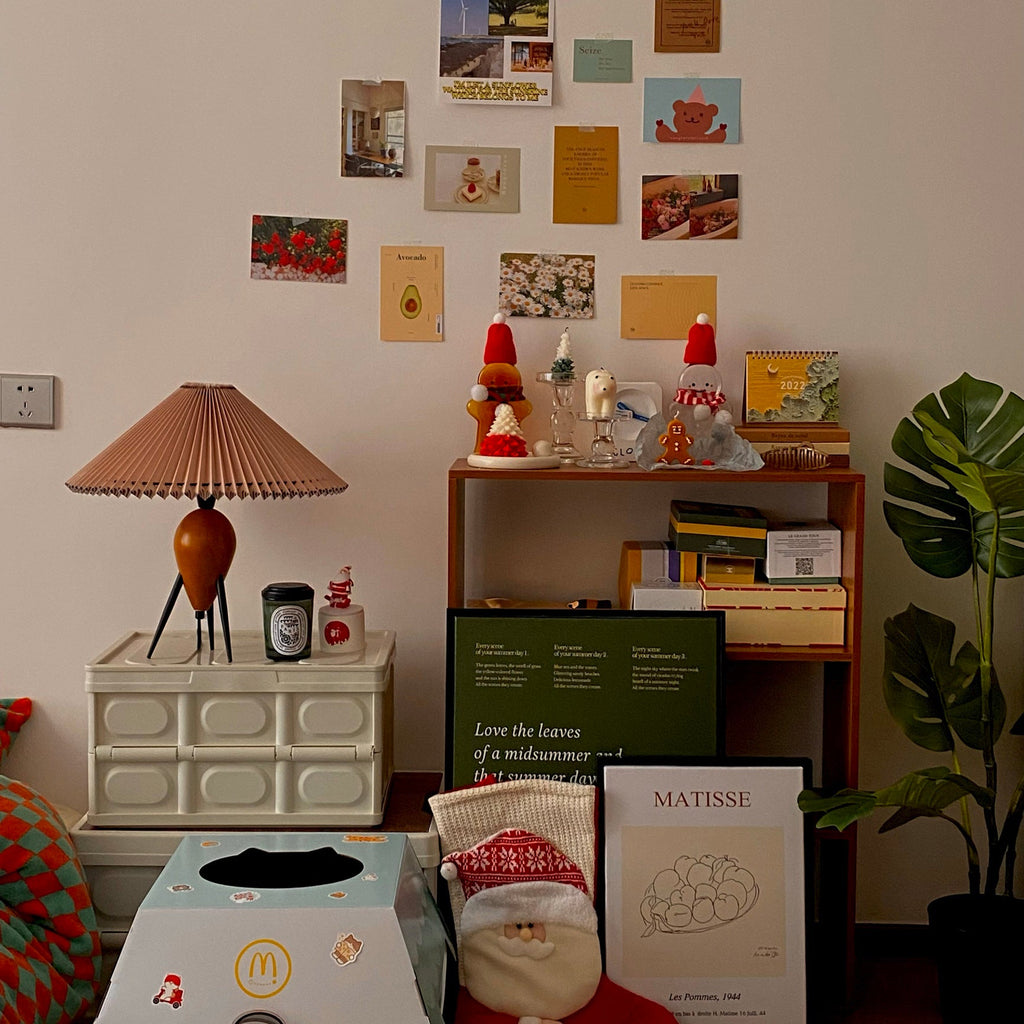 On a pinboard wall of postcards, this Clérachic table lamp stands on a cream drawer unit among festive trinkets and posters.