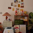 On a pinboard wall of postcards, this Clérachic table lamp stands on a cream drawer unit among festive trinkets and posters.