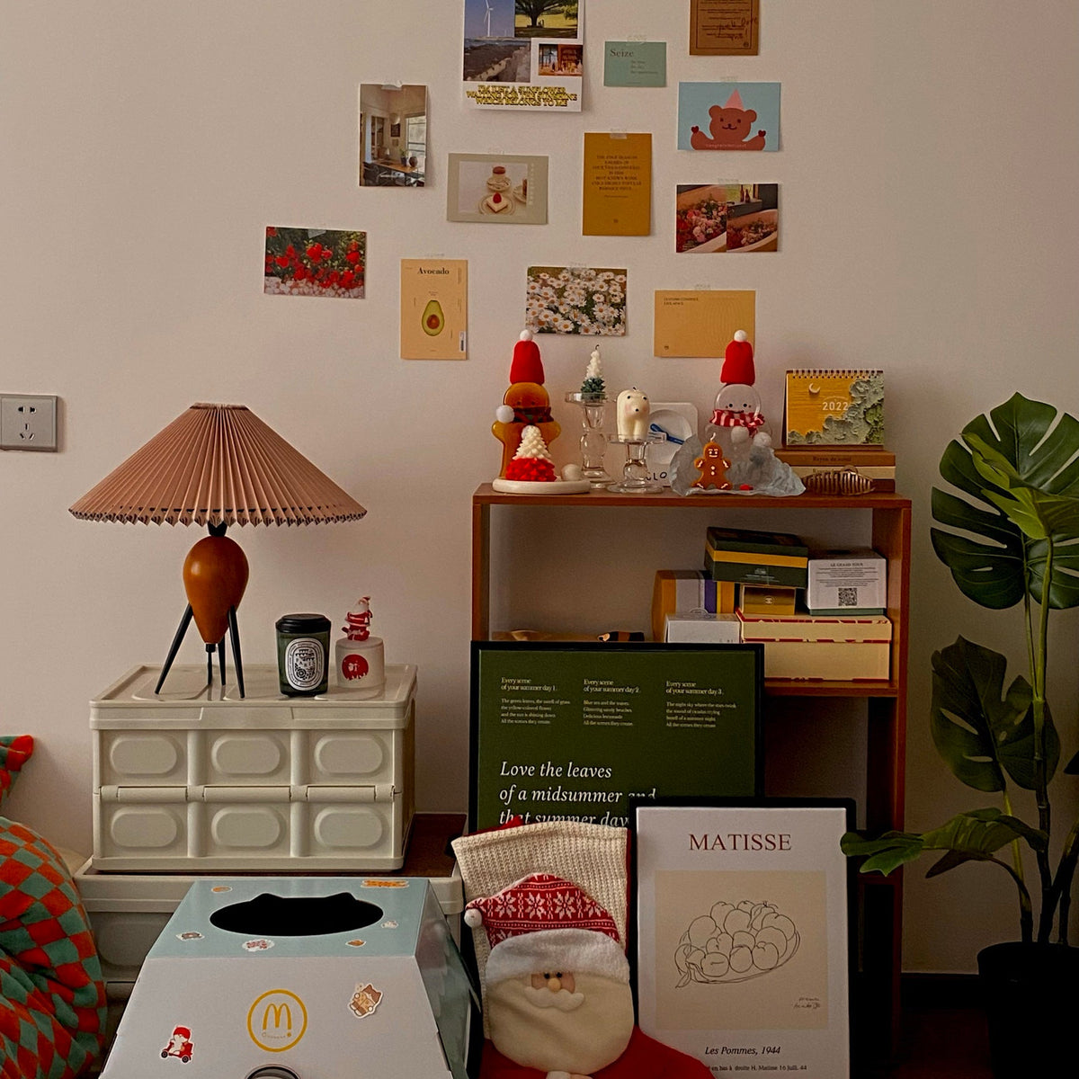 On a pinboard wall of postcards, this Clérachic table lamp stands on a cream drawer unit among festive trinkets and posters.