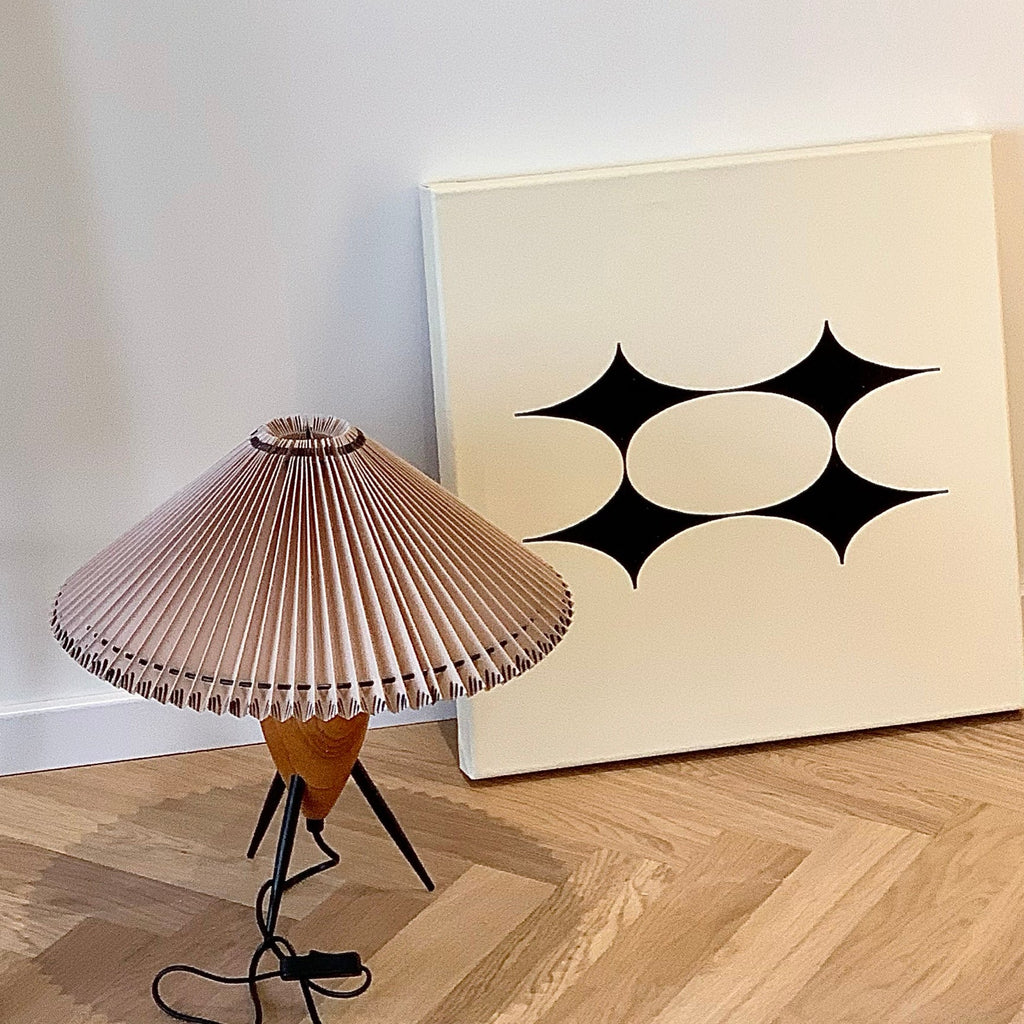 This Clérachic table lamp leans on a bright parquet floor beside a large canvas with a black star pattern.