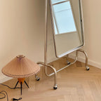 On a parquet floor beside a chrome-framed mirror, this Clérachic table lamp stands with its black cord and plug at its side.