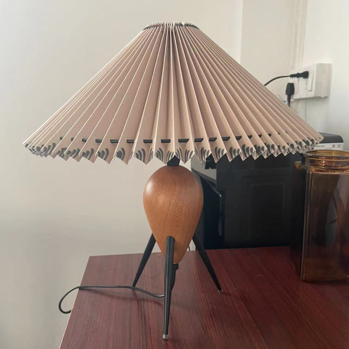 Seen from a low angle, this Clérachic table lamp stands on a dark wood desk, a wall socket and amber jar behind.