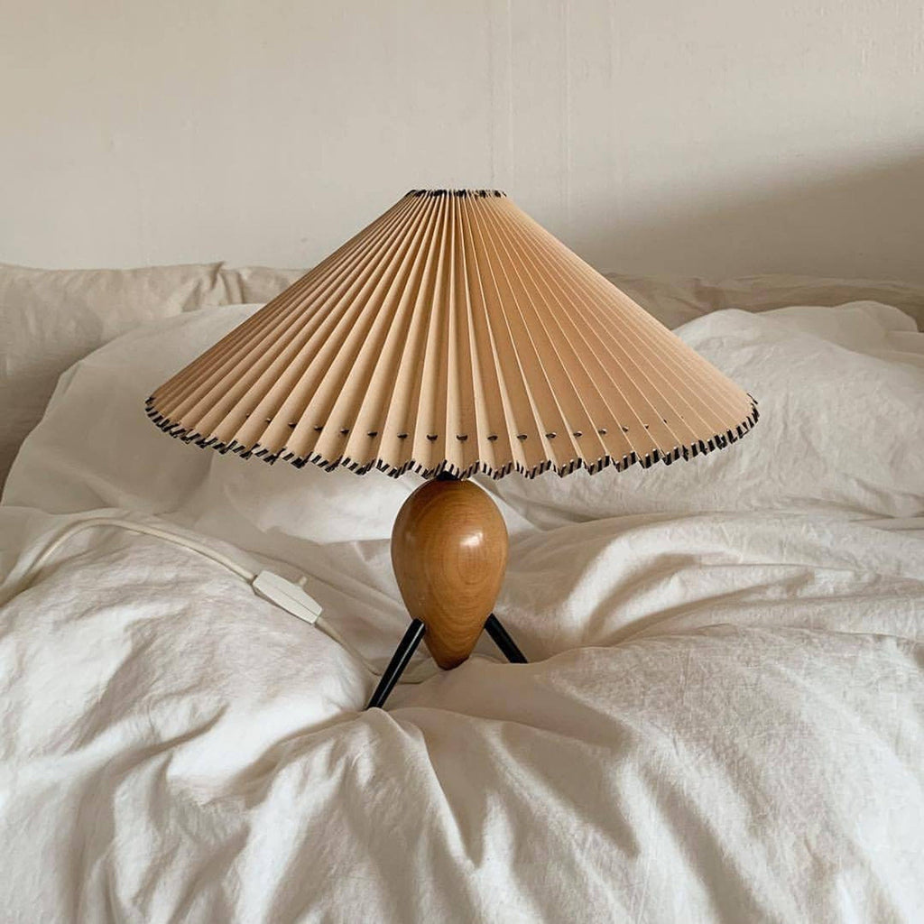 A Clérachic table lamp resting on a rumpled white duvet, its black cord running to an in-line switch.